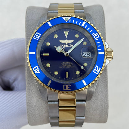 An Invicta dive watch with a blue dial and blue bezel, featuring a two-tone silver and gold stainless steel Oyster bracelet, displayed on a gray stand.