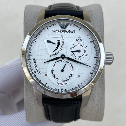 An Emporio Armani watch with a silver stainless steel case, white dial, black leather strap, and black bezel, displayed on a light gray stand.