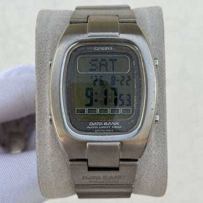A Casio Data Bank titanium analog-digital watch with a brushed silver-tone metal case and bracelet, displayed on a light gray velvet wrist strap. The watch features a square digital LCD screen showing the time as 9:17 and the day as SAT.